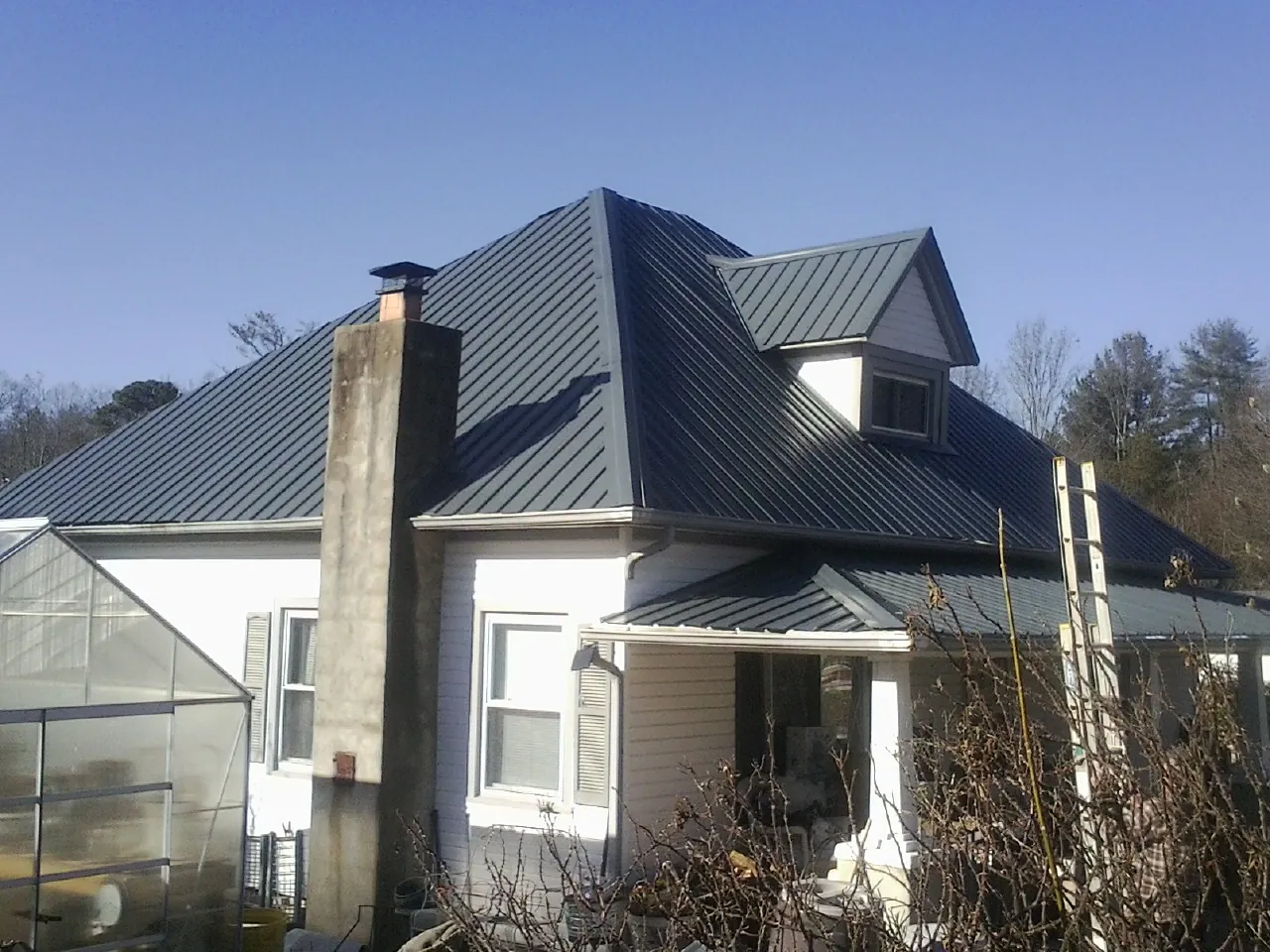 Dark blue standing seam metal roof on a white farmhouse with dormer — Slate & Tile Roof Repair by Roofing Brothers in Muenster