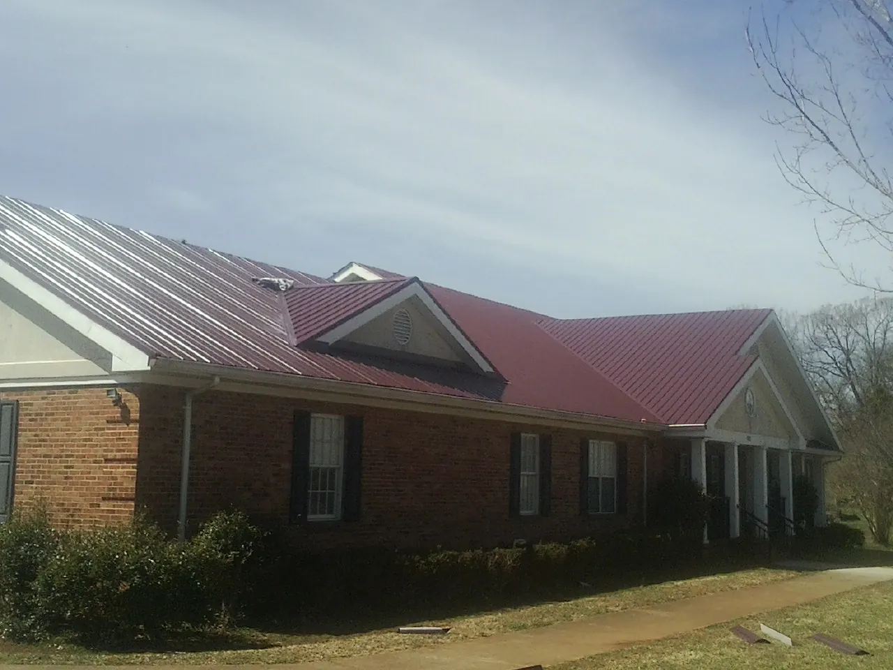 Red metal roof with gabled entries on a long brick building, from a Hail Damage Roof Repair job in Muenster