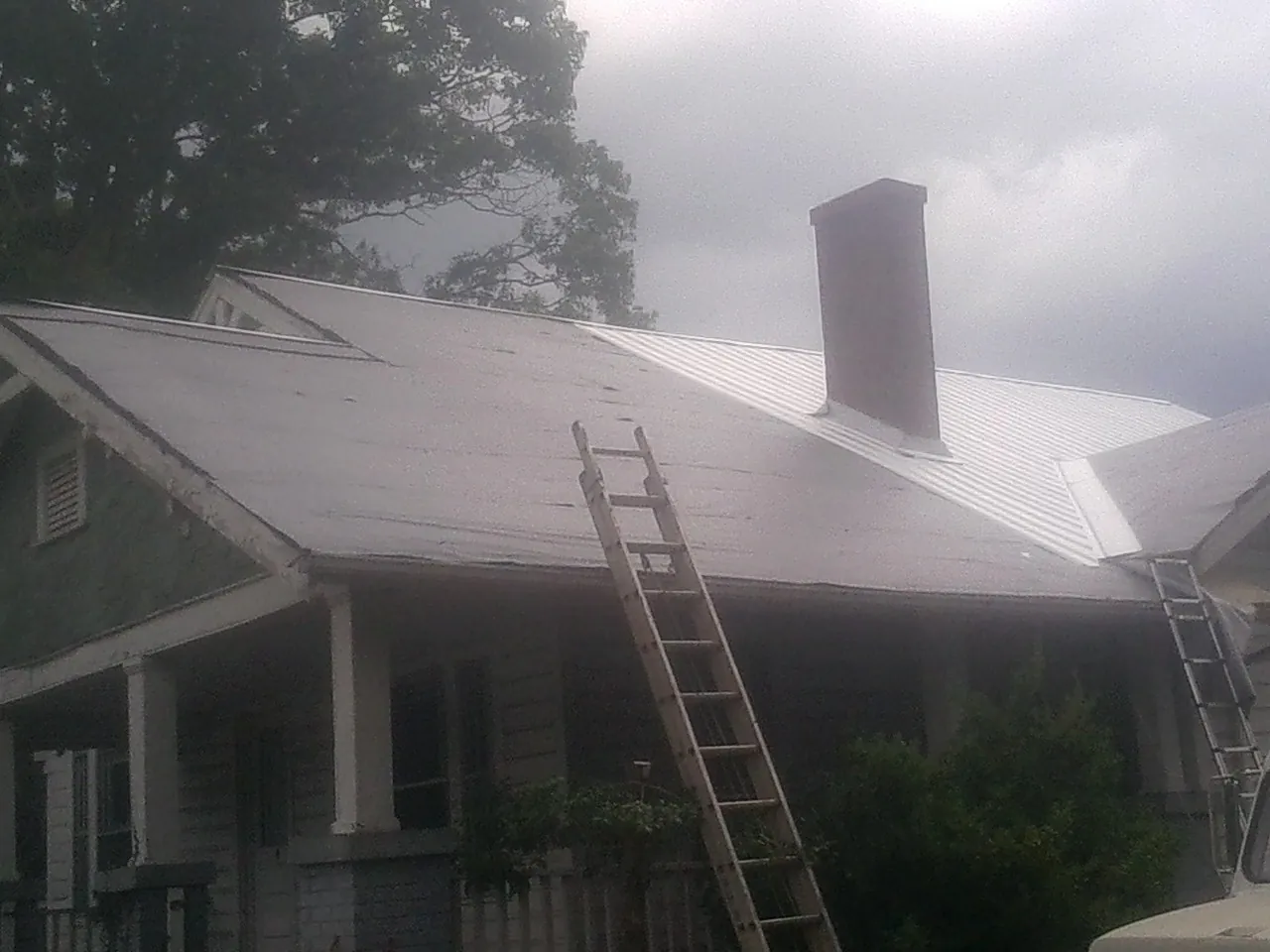 Ladders against a metal roof on an older home with a brick chimney in Muenster