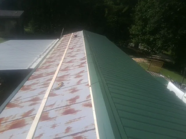 Old rusted panels beside newly installed green metal roofing — Wind Damage Roof Repair by Roofing Brothers in Muenster
