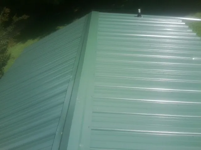New green metal panels meeting at the ridge of a roof — Flat Roof Repair work by our crew in Muenster