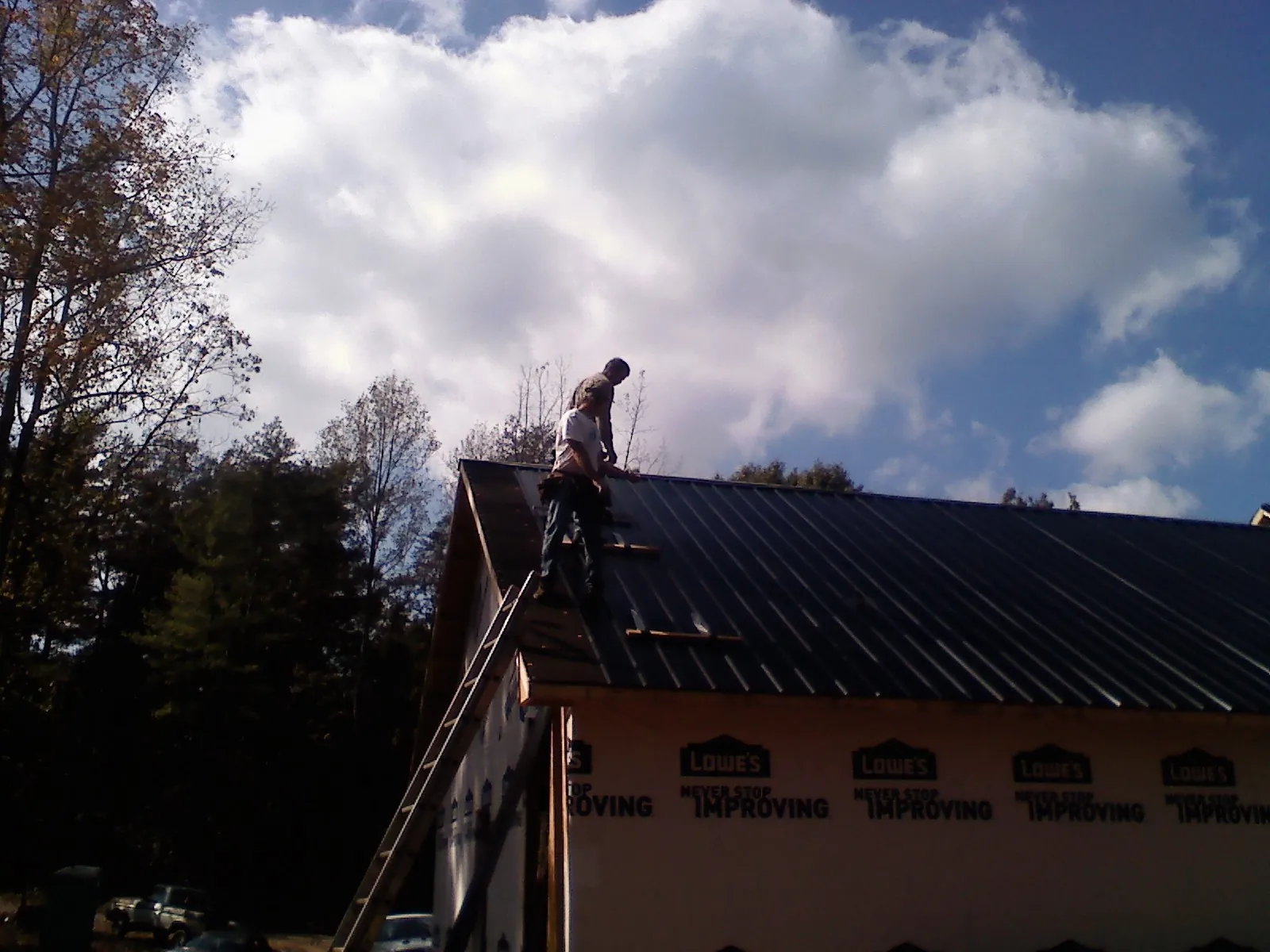 Roofer fastening dark metal panels high against a cloudy sky, from a Roof Inspection job in Muenster