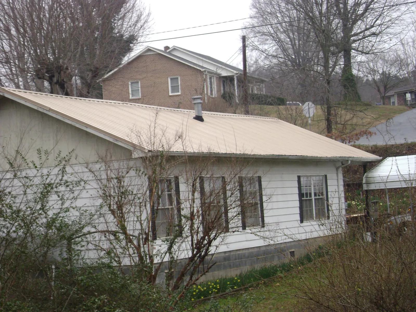 Tan metal roof on a white sided house set into a hillside — Commercial Roofing by Roofing Brothers in Muenster